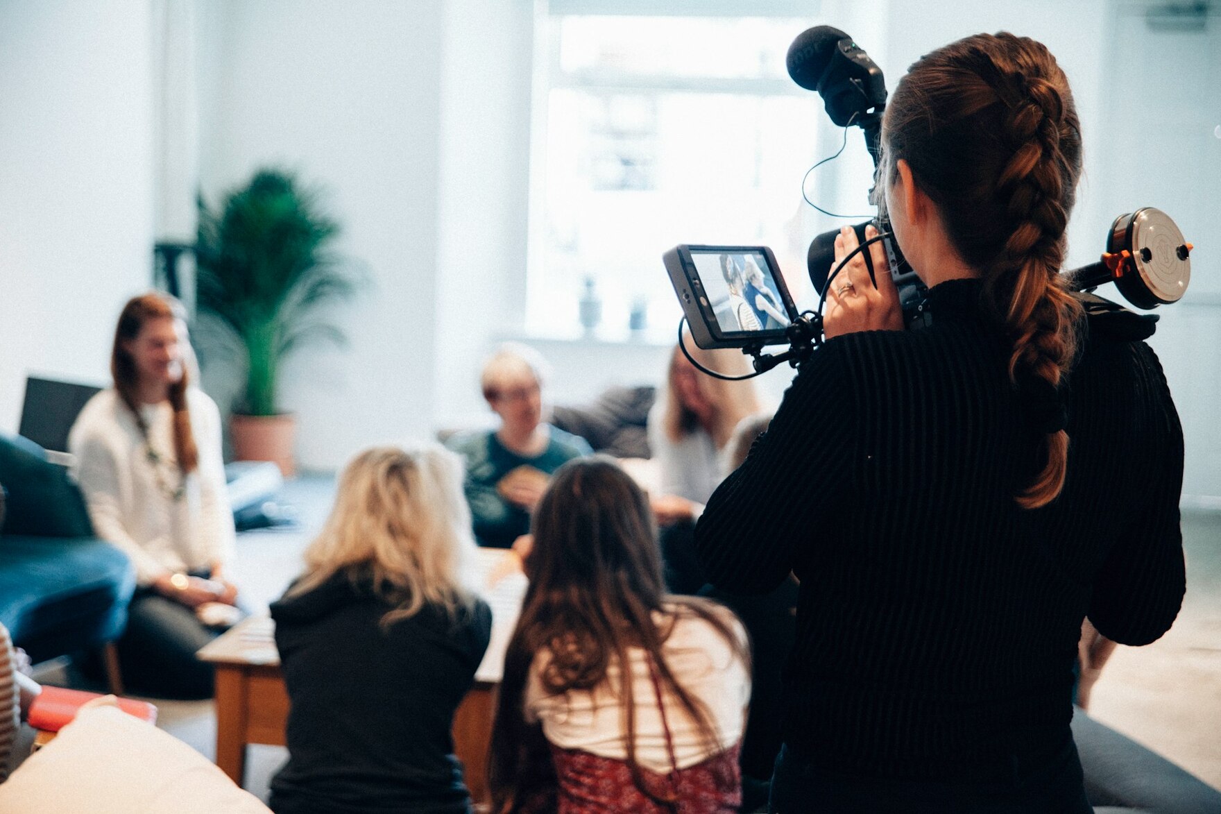 Ein Foto von einer Pressekonferenz, verwischt zu sehen. Im Vordergrund ist gut zu sehen: Eine Kamerafrau mit einer Kamera in der Hand, auf die Konferenz gerichtet.