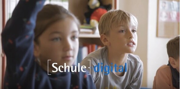 Ausschnitt aus einem Klassenzimmer: Ein Mädchen meldet sich, ein Junge schaut interessiert. In der Mitte des Bildes steht "Schule digital".
