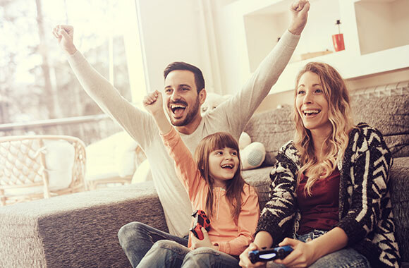Eine Familie (Vater, Mutter, Kind) spielen gemeinsam ein Videospiel.